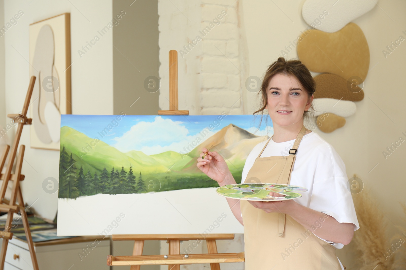 Photo of Portrait of smiling woman drawing landscape with brush in studio