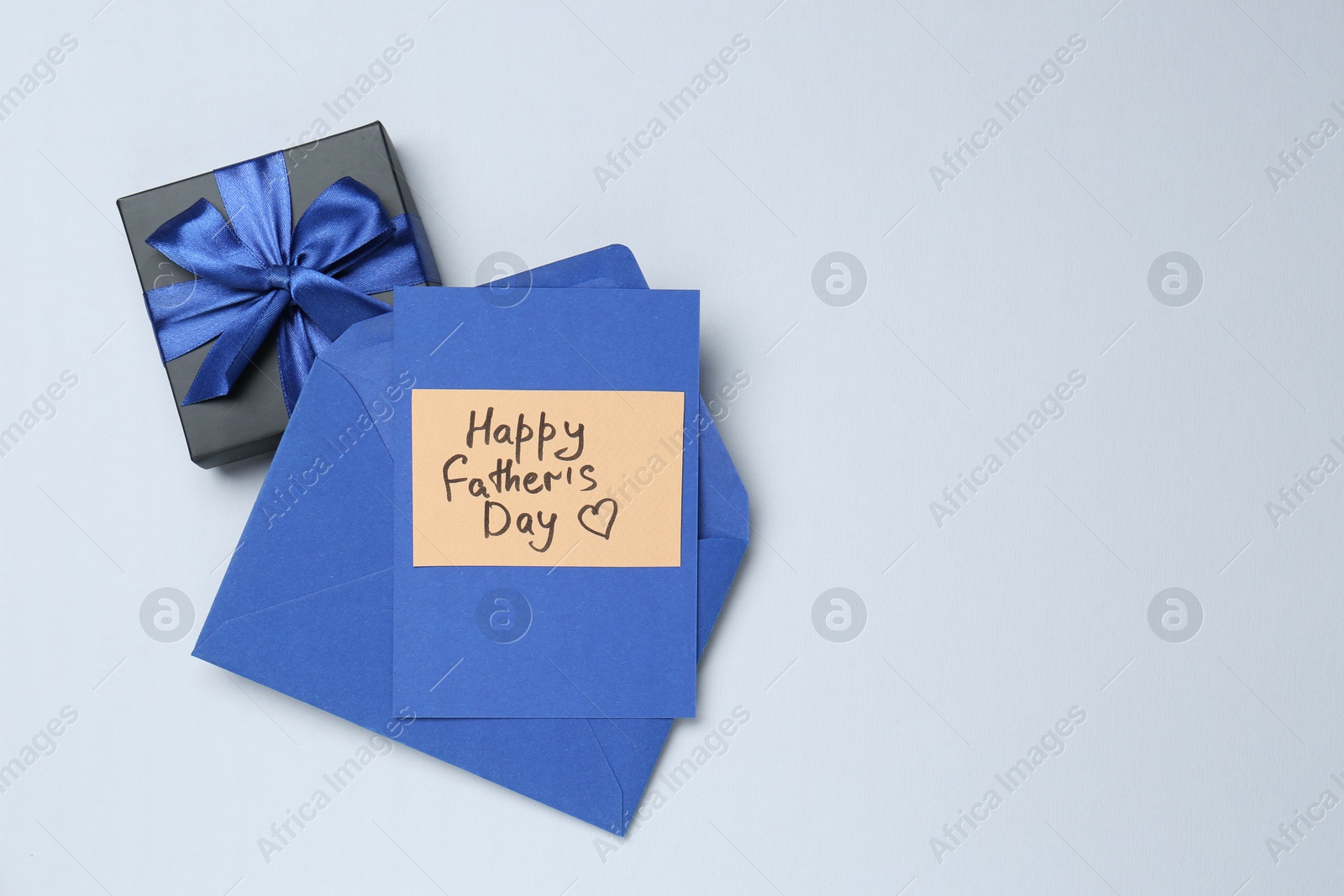 Photo of Greeting card with phrase Happy Father's Day, envelope and gift on light background, top view. Space for text