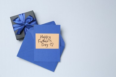 Photo of Greeting card with phrase Happy Father's Day, envelope and gift on light background, top view. Space for text