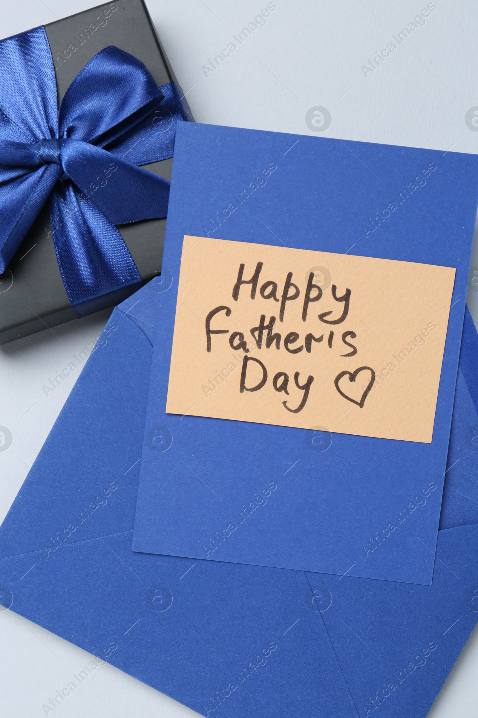 Photo of Greeting card with phrase Happy Father's Day, envelope and gift on light background, top view