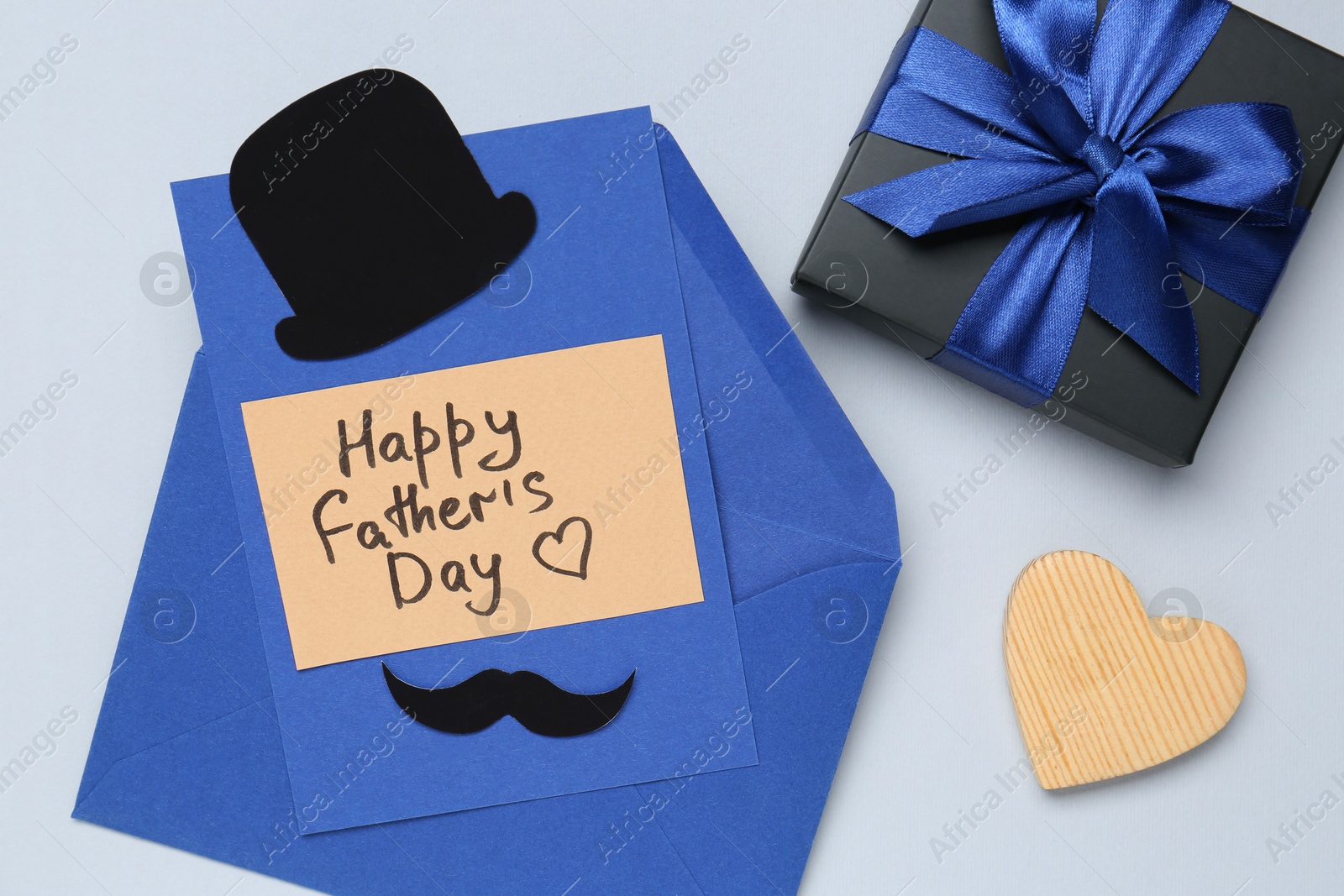 Photo of Greeting card with phrase Happy Father's Day, envelope, wooden heart and gift on light background, top view