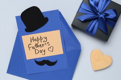 Photo of Greeting card with phrase Happy Father's Day, envelope, wooden heart and gift on light background, top view