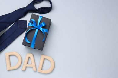 Happy Father's Day. Word Dad made with wooden letters, gift and tie on light background, flat lay. Space for text