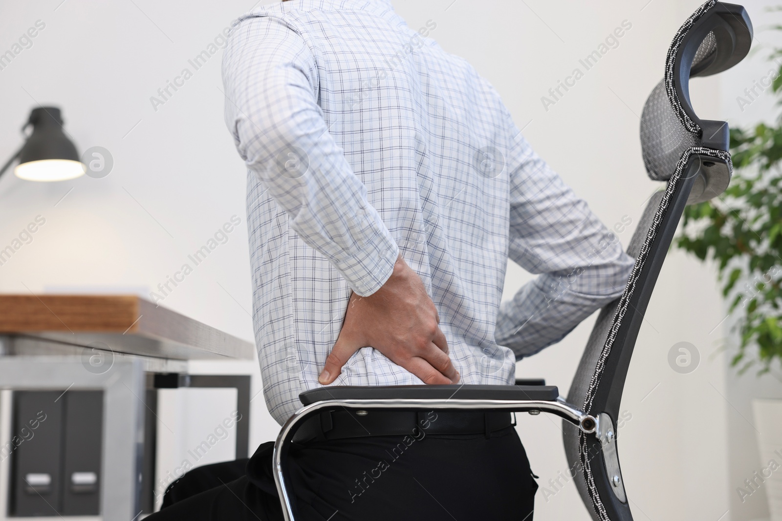 Photo of Man suffering from back pain in office, closeup. Symptom of poor posture
