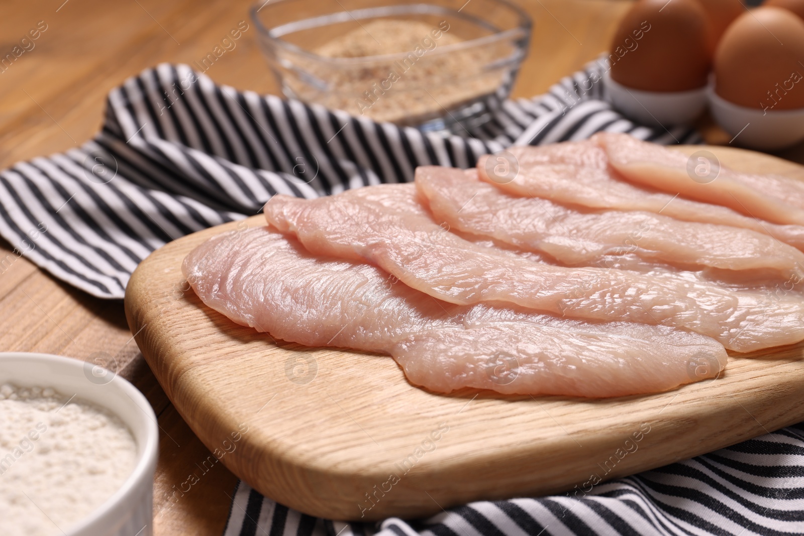 Photo of Cooking schnitzel. Raw meat, flour, eggs and breadcrumbs on wooden table, closeup