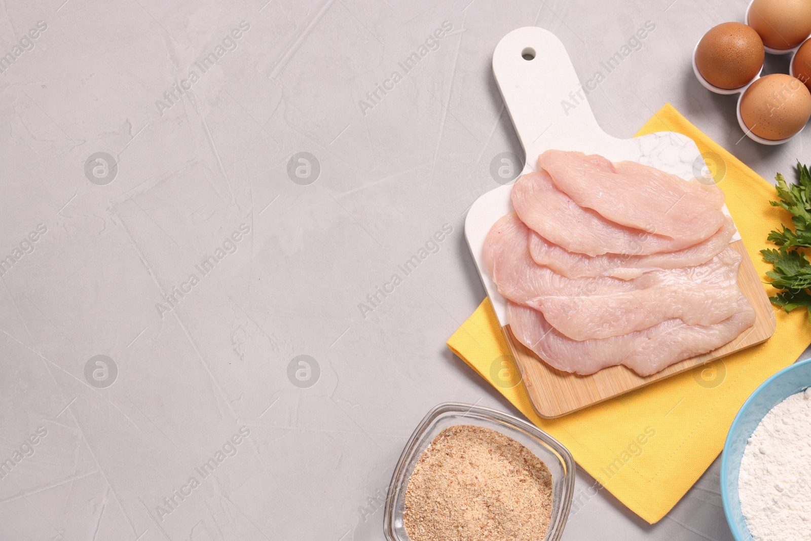 Photo of Cooking schnitzel. Raw meat, flour, eggs and breadcrumbs on light grey table, top view. Space for text