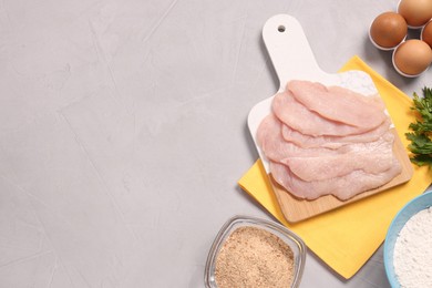 Photo of Cooking schnitzel. Raw meat, flour, eggs and breadcrumbs on light grey table, top view. Space for text