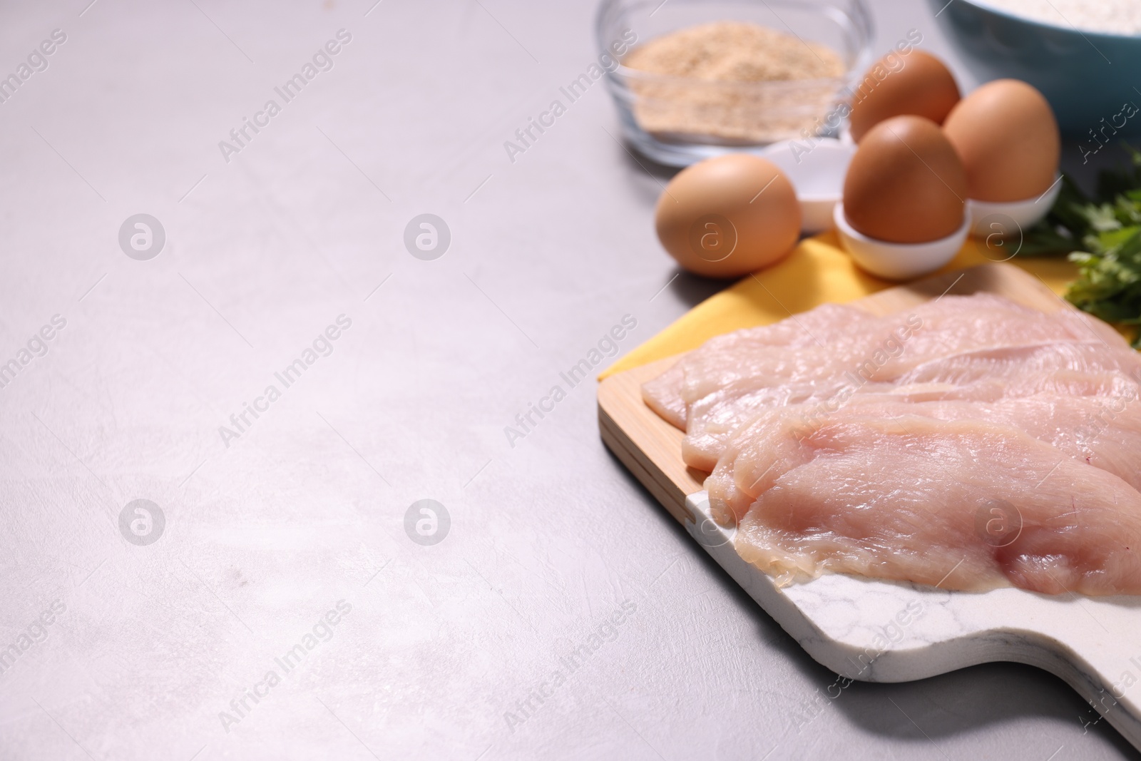 Photo of Cooking schnitzel. Raw meat, eggs and breadcrumbs on light grey table, space for text