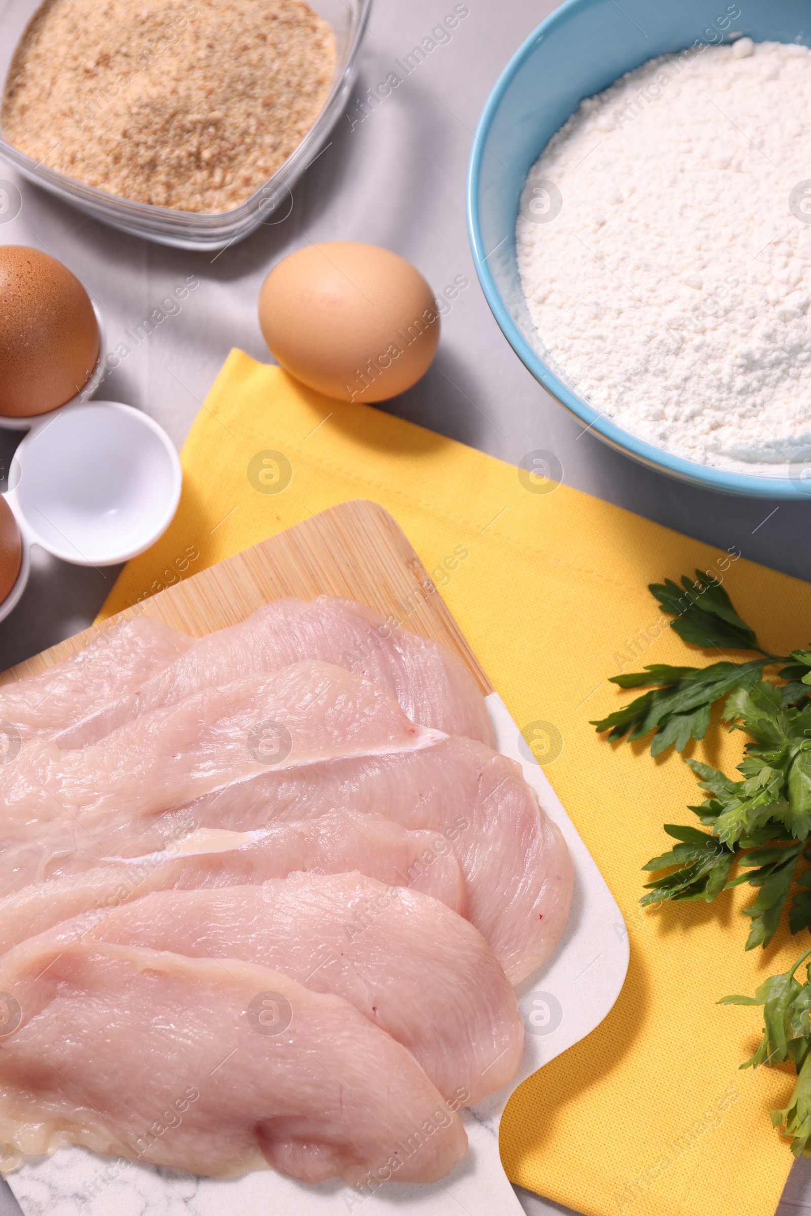 Photo of Cooking schnitzel. Raw meat, flour, eggs, breadcrumbs and parsley on light grey table, top view