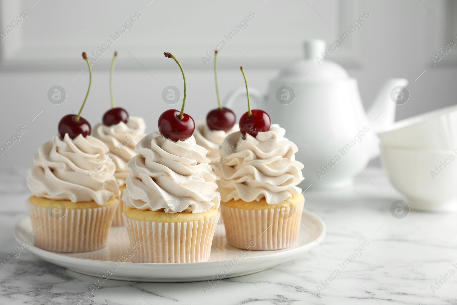 Photo of Delicious cupcakes with cream and cherries on white marble table