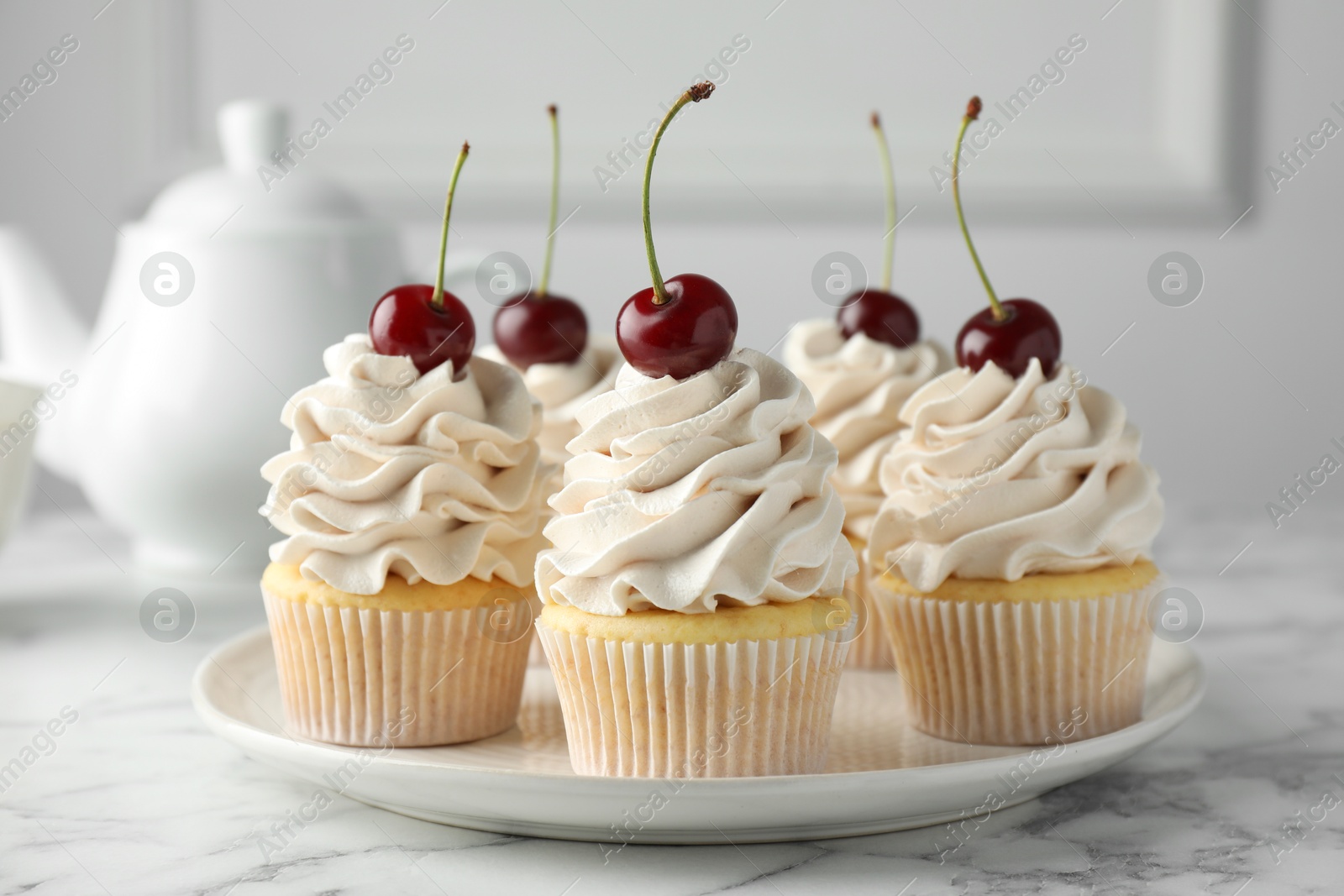 Photo of Delicious cupcakes with cream and cherries on white marble table