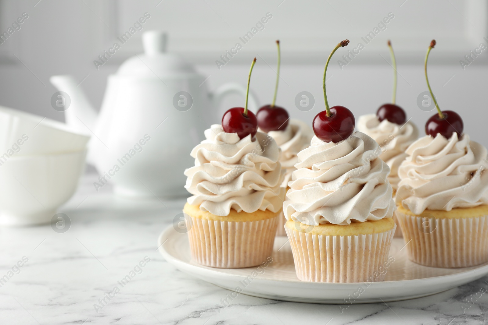 Photo of Delicious cupcakes with cream and cherries on white marble table