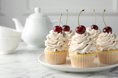 Delicious cupcakes with cream and cherries on white marble table