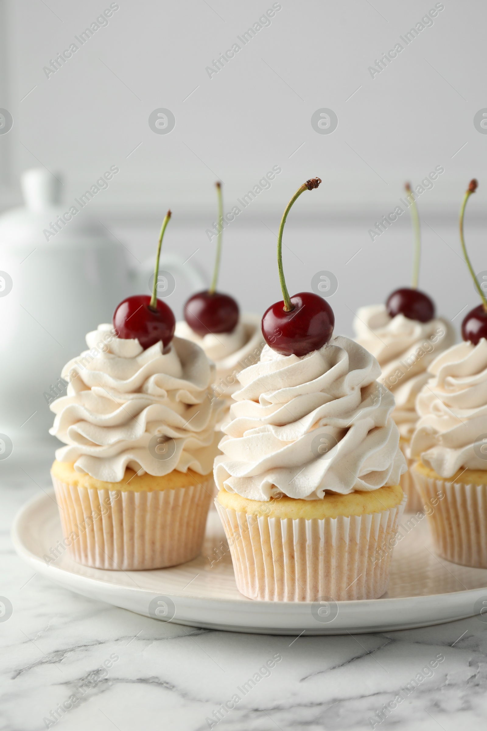 Photo of Delicious cupcakes with cream and cherries on white marble table