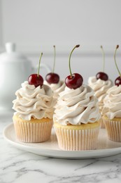 Delicious cupcakes with cream and cherries on white marble table