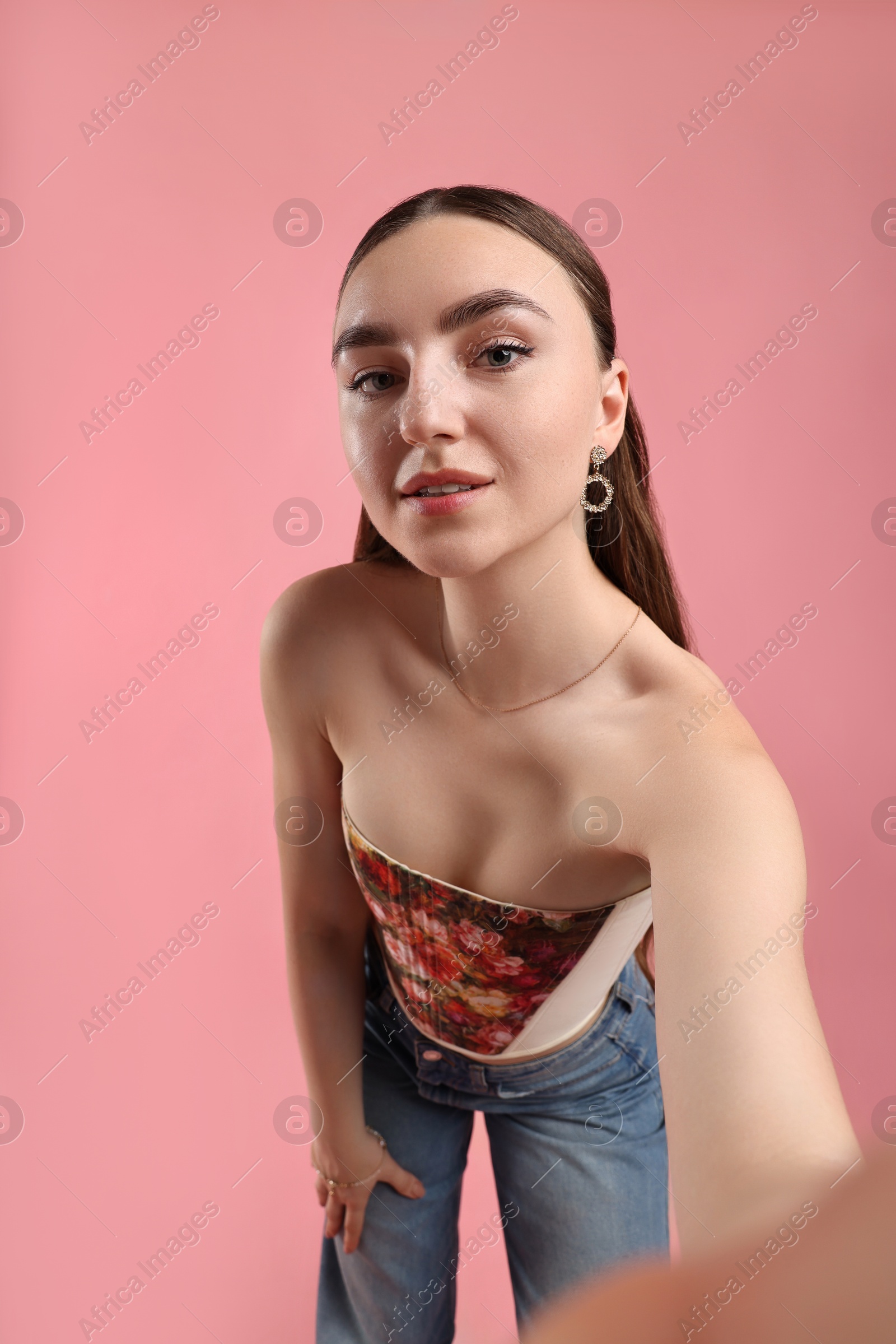 Photo of Smiling woman in stylish corset taking selfie on pink background