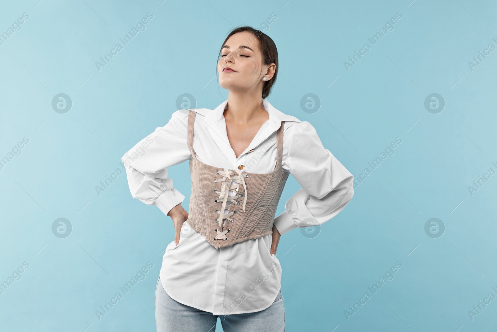 Photo of Beautiful woman in stylish corset posing on light blue background