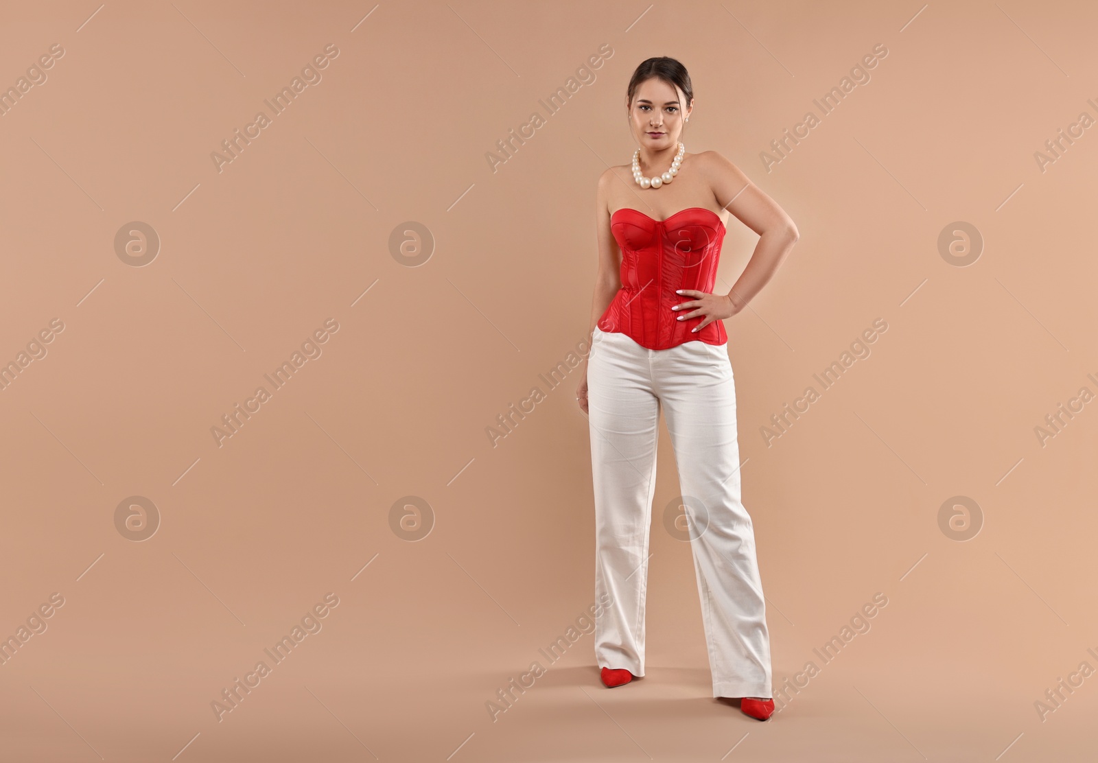 Photo of Beautiful woman in red corset posing on beige background. Space for text