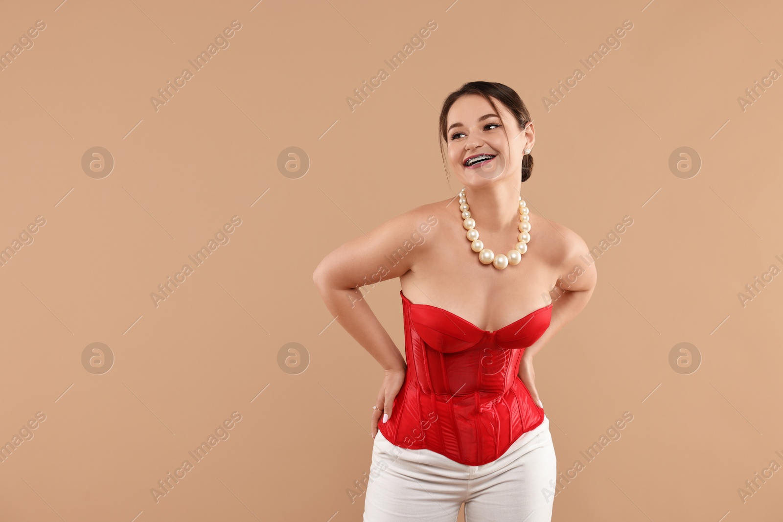 Photo of Smiling woman in red corset posing on beige background. Space for text