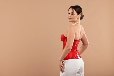 Beautiful woman in red corset posing on beige background, back view. Space for text