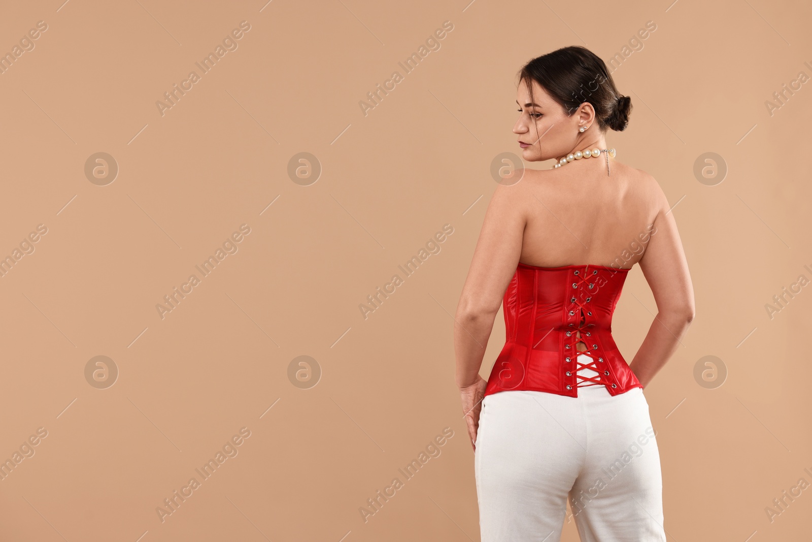 Photo of Beautiful woman in red corset posing on beige background, back view. Space for text