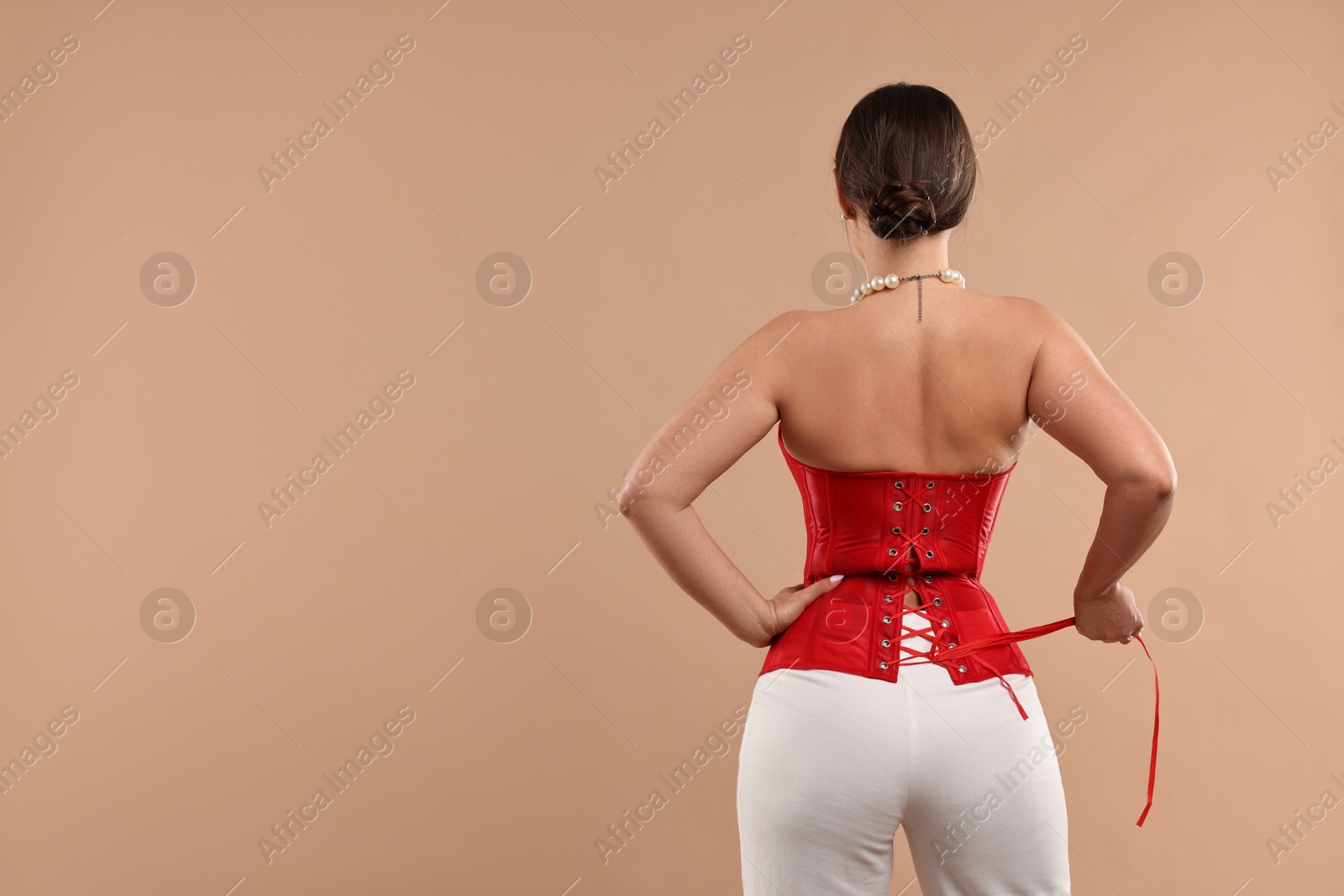 Photo of Woman in red corset posing on beige background, back view. Space for text