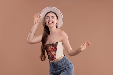 Smiling woman in stylish corset and hat posing on beige background