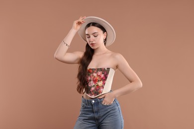 Photo of Beautiful woman in stylish corset and hat posing on beige background