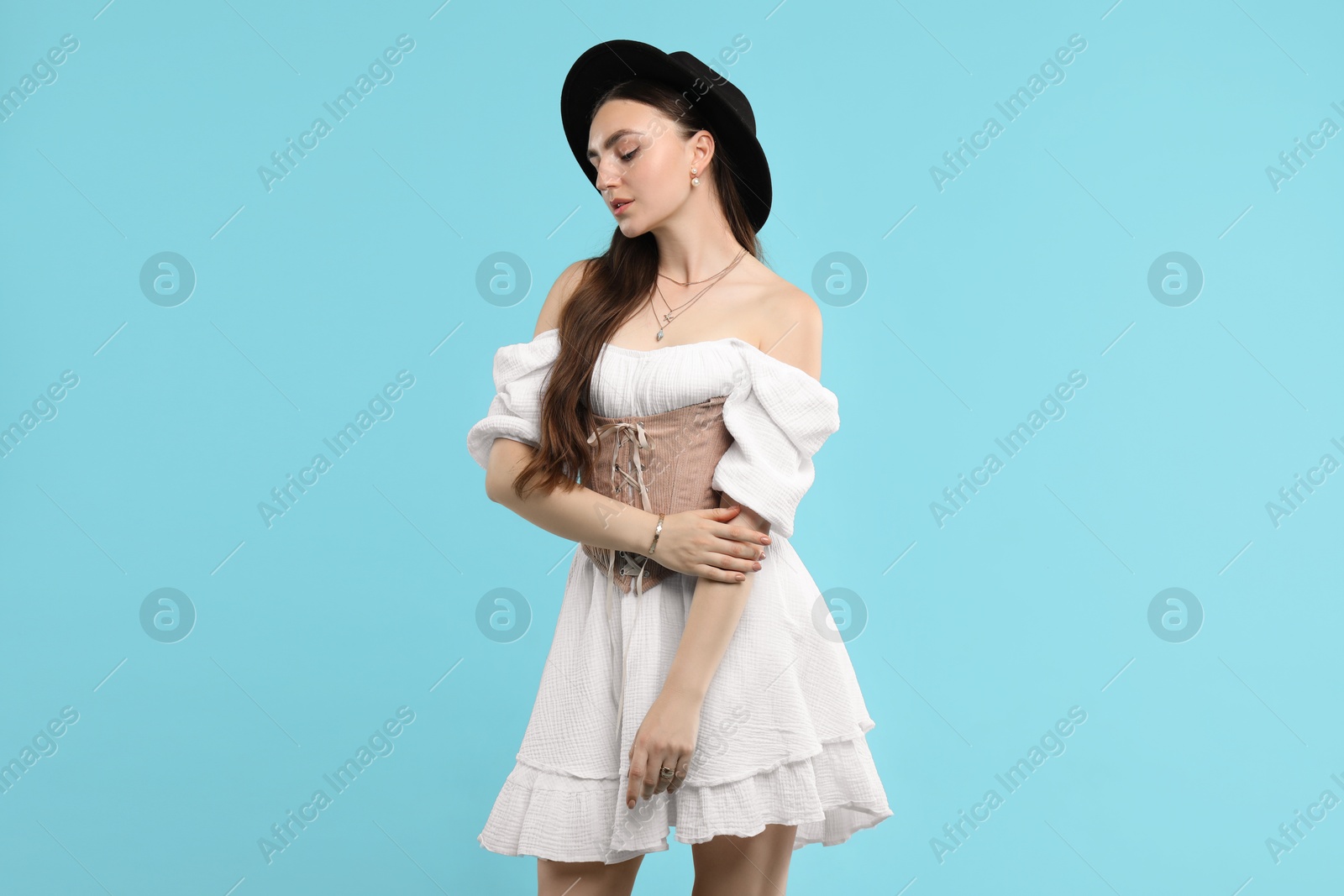 Photo of Beautiful woman in velvet corset and hat posing on light blue background