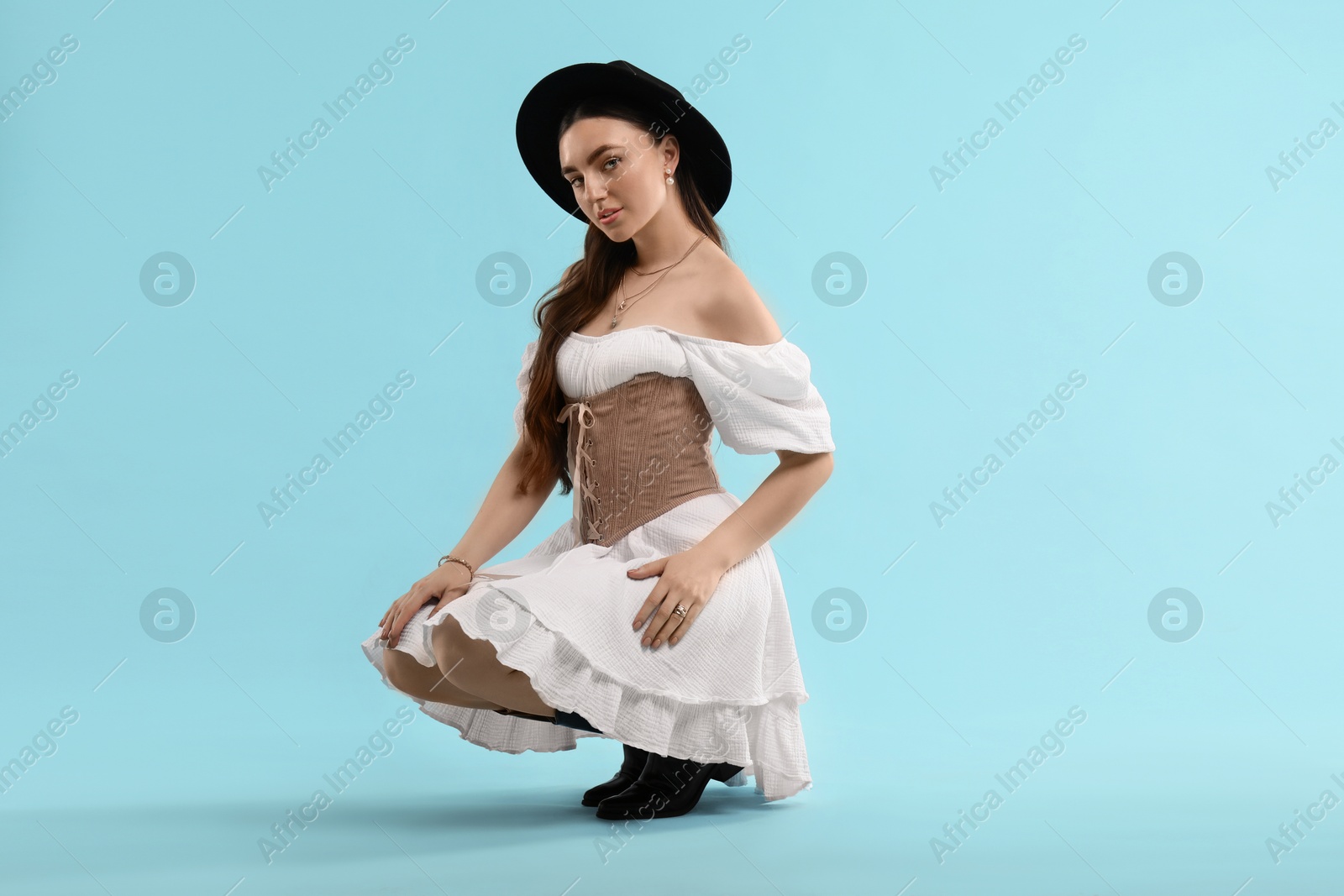 Photo of Beautiful woman in velvet corset and hat posing on light blue background