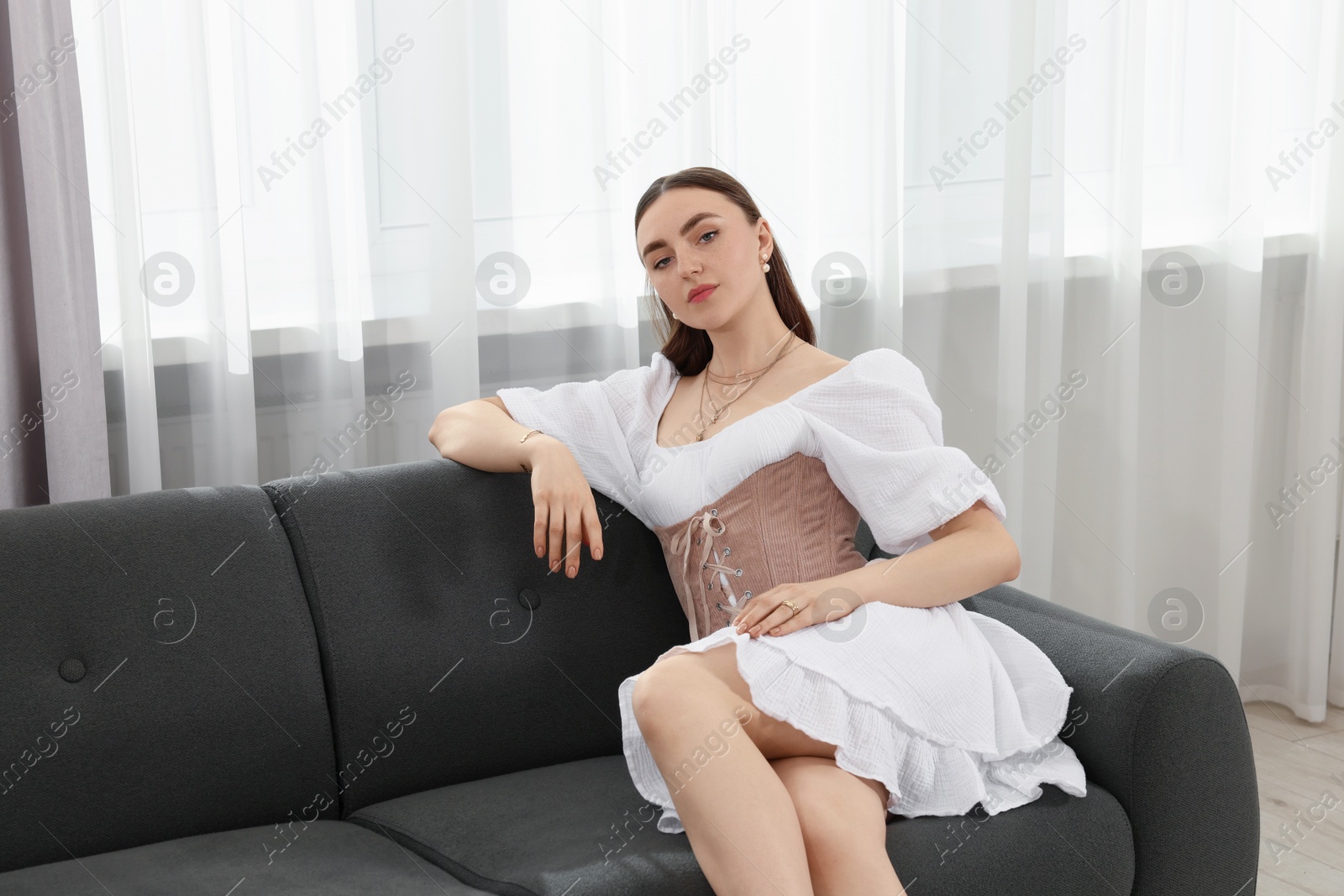 Photo of Beautiful woman in stylish corset sitting on sofa indoors