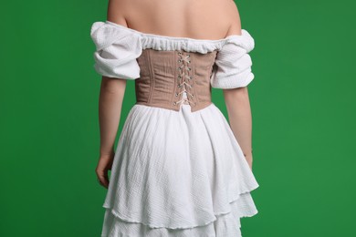 Photo of Woman in stylish corset on green background, back view
