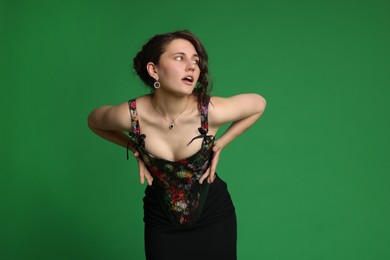 Beautiful woman in stylish corset posing on green background