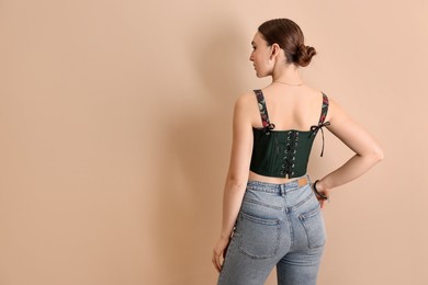 Photo of Woman in stylish corset on beige background, back view. Space for text