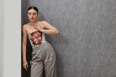 Beautiful young woman in stylish corset near grey wall, space for text