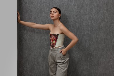 Photo of Beautiful young woman in stylish corset near grey wall