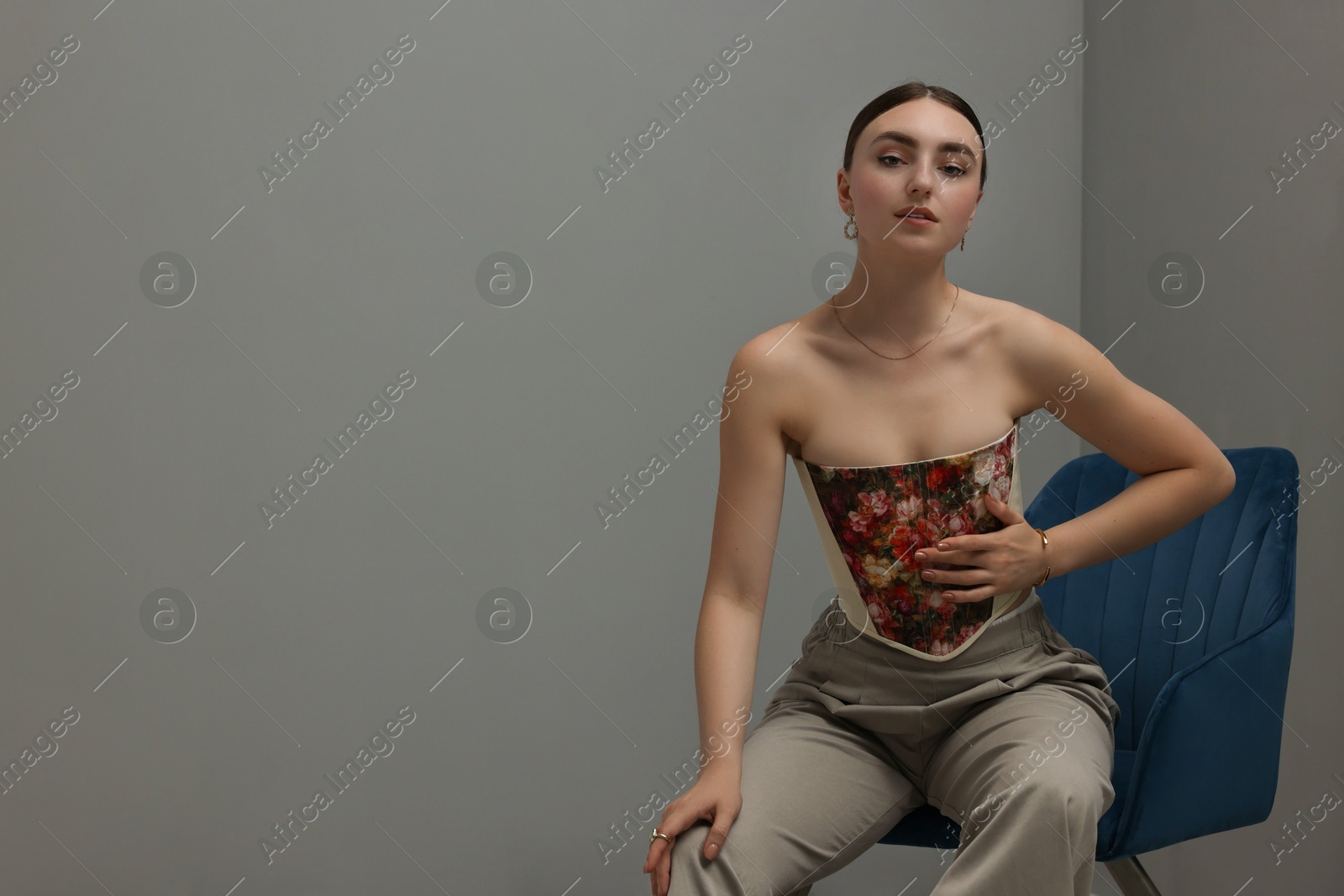 Photo of Beautiful young woman in stylish corset on armchair indoors, space for text