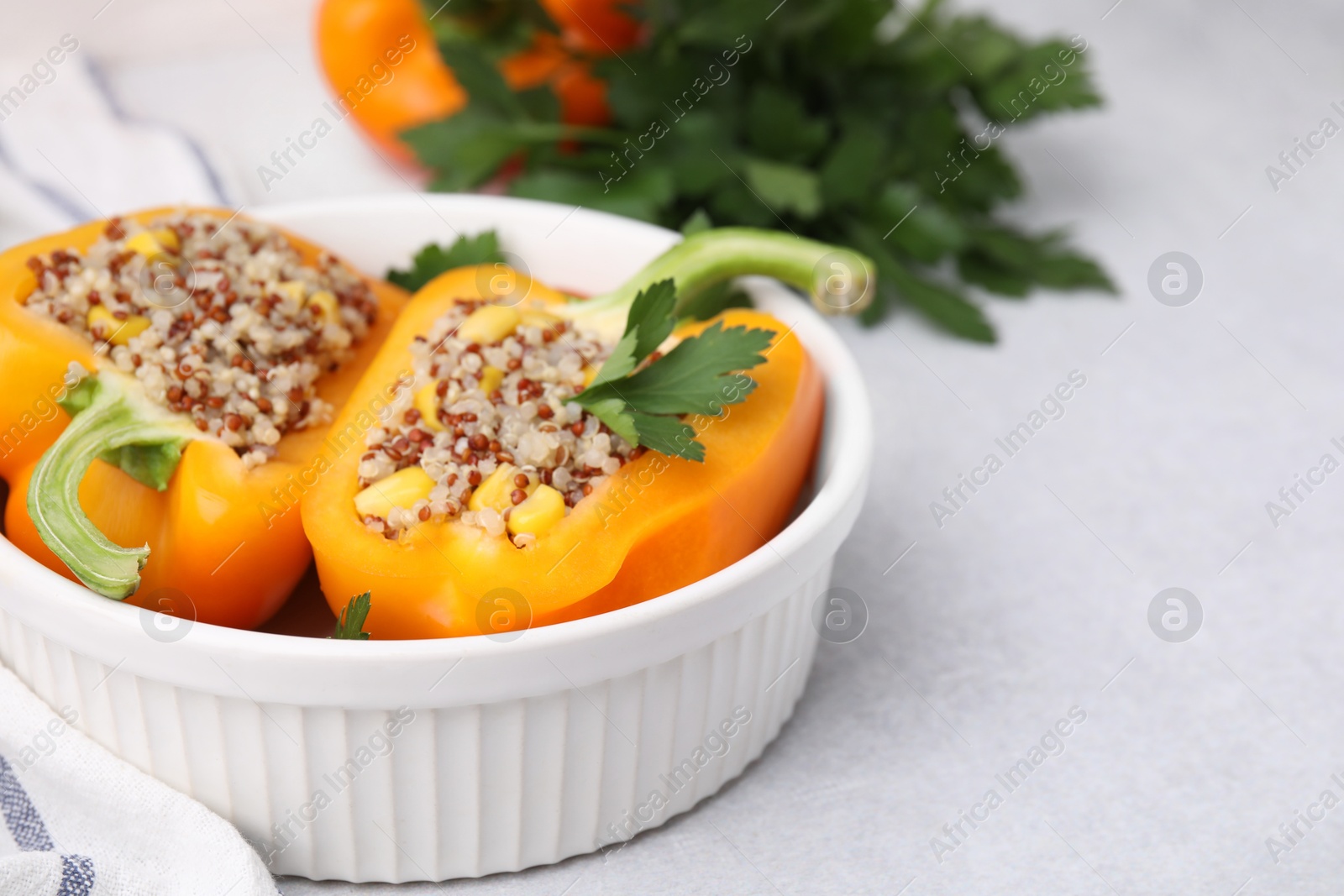 Photo of Quinoa stuffed bell pepper and parsley in bowl on light table, closeup. Space for text