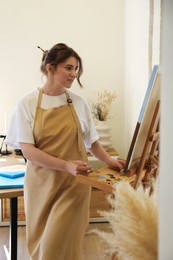 Photo of Woman drawing on easel with canvas in studio