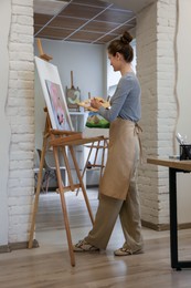 Woman drawing on easel with canvas in studio