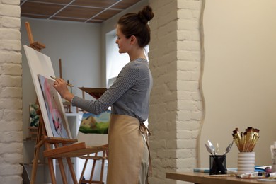 Photo of Woman drawing on easel with canvas in studio