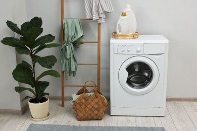 Photo of Washing machine, detergents, houseplant and ladder in laundry room