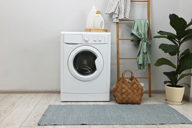 Photo of Washing machine, detergents, houseplant and ladder in laundry room