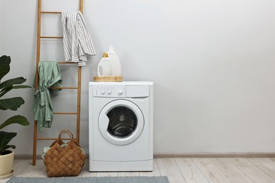 Photo of Washing machine, detergents, houseplant and ladder in laundry room, space for text