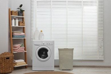 Photo of Washing machine, detergents, towels and baskets in laundry room