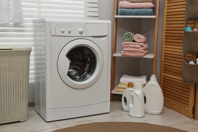 Photo of Washing machine, detergents, towels and basket in laundry room