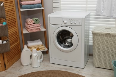 Photo of Washing machine, detergents, towels and basket in laundry room