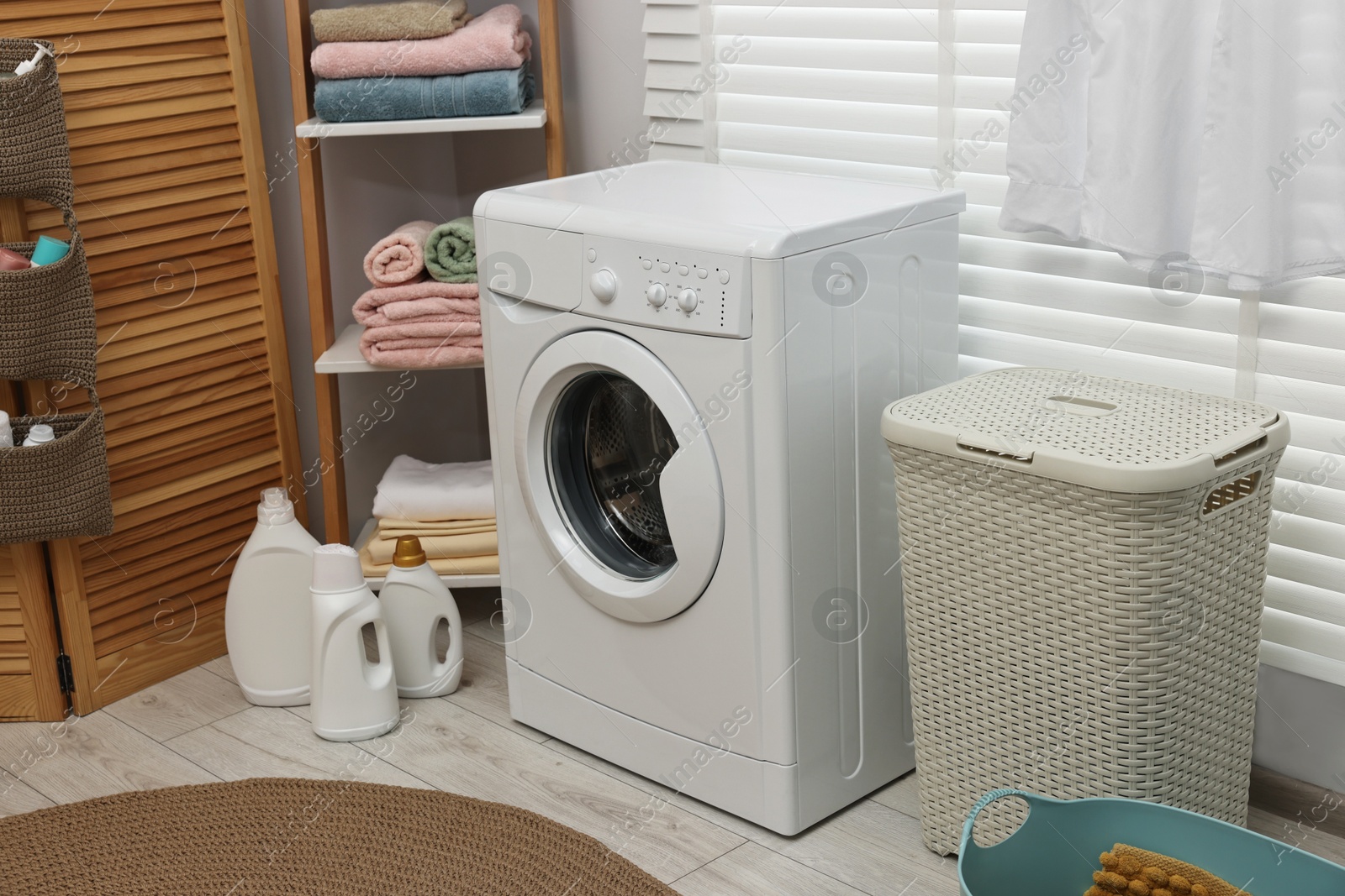 Photo of Washing machine, detergents, towels and basket in laundry room