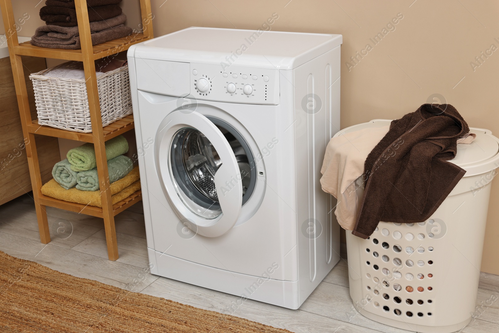 Photo of Washing machine, basket and shelving unit near beige wall indoors