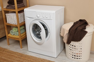 Photo of Washing machine, basket and shelving unit near beige wall indoors